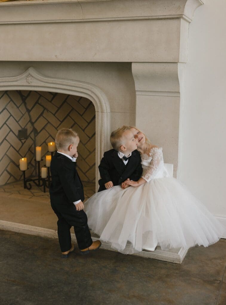 Three little kids sit together on a fireplace before the wedding ceremony